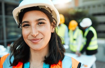 Mujer orgullosa con un casco y chaleco en una obra en construcción