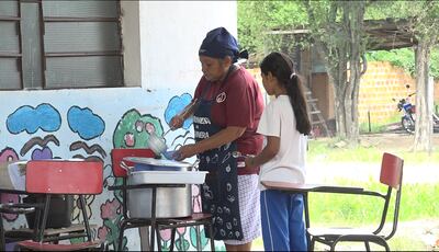 Una mamá, contratada por la proveedora de Hambre Cero, sirve un plato de almuerzo escolar a una estudiante.