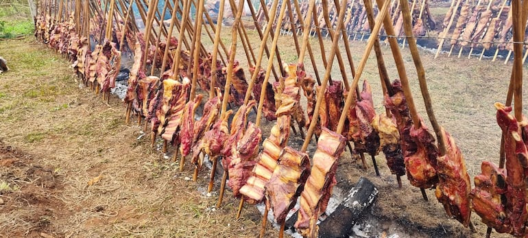 Piezas de carne asadas colgadas en estacas en un entorno rural, sin personas visibles en la imagen.