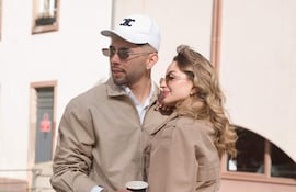 Pareja sonriente junto al canal, el hombre con chaqueta beige y gorro blanco, la mujer con chaqueta beige y jeans oscuros.