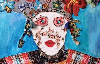 Obra artística con un rostro femenino estilizado, fondo azul y adornos bordados de flores vibrantes.