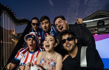 Lucas Zaracho con sombrero y camiseta roja y blanca, Jazmín del Paraguay en vestido brillante, celebran juntos en un escenario festivo.
