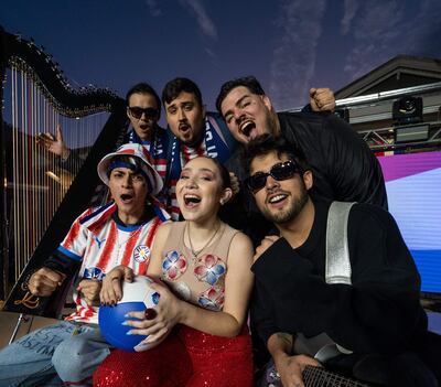 Lucas Zaracho con sombrero y camiseta roja y blanca, Jazmín del Paraguay en vestido brillante, celebran juntos en un escenario festivo.