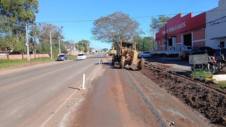 Escena de construcción en carretera con maquinaria amarilla, vehículos circulando y letrero de Grupo Vera e Hijos al fondo.