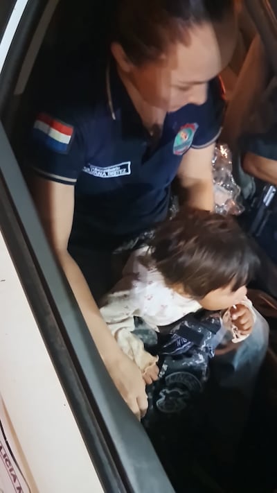 Una oficial de Policía sostiene en su regazo a la beba segundos después de ser encontrada en precaria casillita de madera.