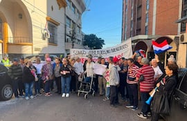Grupo de jubilados con pancartas que dicen 'SOMOS JUBILADOS, NO MENDIGOS' frente a un edificio, en un ambiente de protesta.