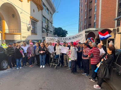 Grupo de jubilados con pancartas que dicen 'SOMOS JUBILADOS, NO MENDIGOS' frente a un edificio, en un ambiente de protesta.