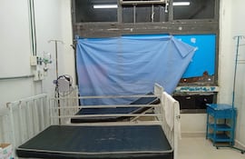 Sala de hospital con dos camas vacías y un carrito azul, luz natural y ambiente deteriorado.