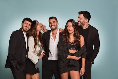 Cinco personas sonrientes en fondo azul: hombre barbudo con saco negro y camiseta blanca, mujer con camisa blanca y corbata, otro hombre robusto y mujer con blusa negra.