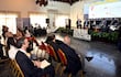 Nueve personas en sala de conferencias, un orador gesticulando mientras los demás escuchan con atención, fondo de presentación sobre energía.
