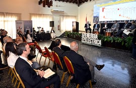 Nueve personas en sala de conferencias, un orador gesticulando mientras los demás escuchan con atención, fondo de presentación sobre energía.