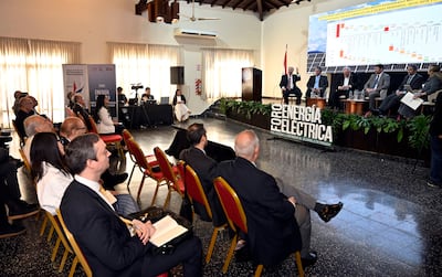 Nueve personas en sala de conferencias, un orador gesticulando mientras los demás escuchan con atención, fondo de presentación sobre energía.