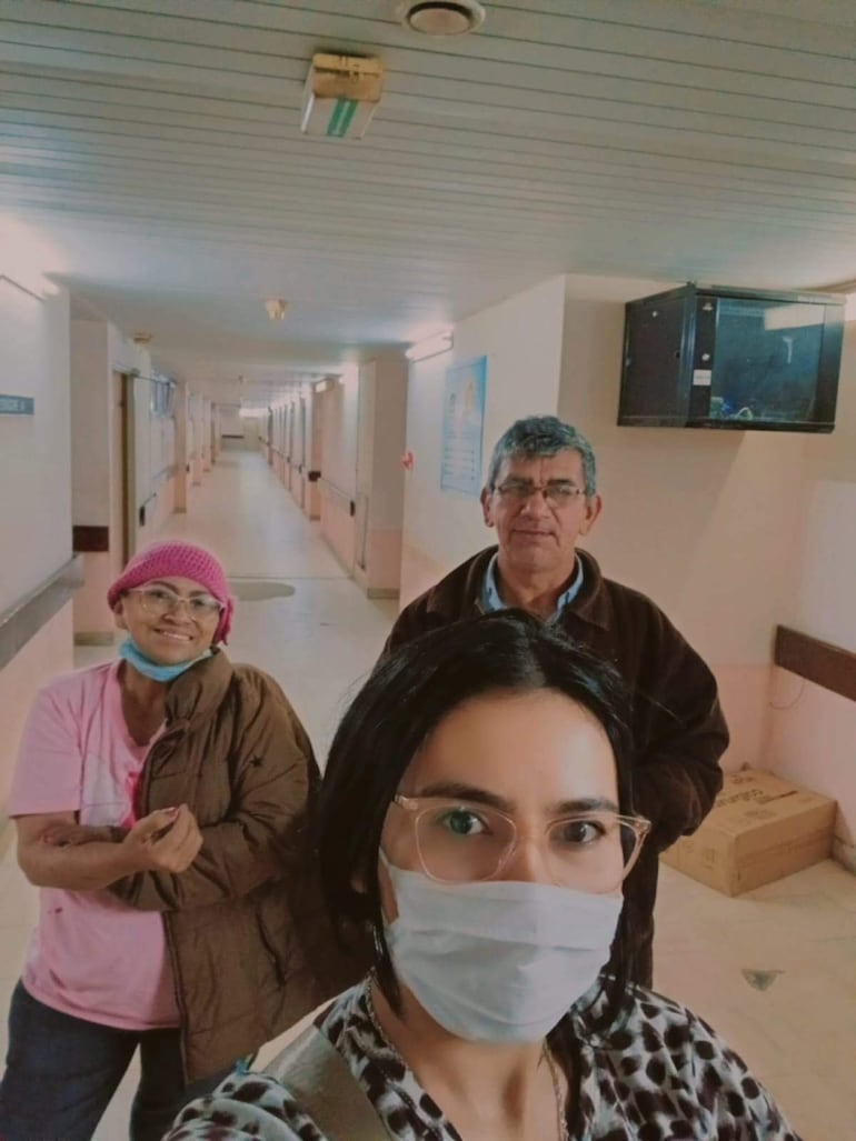 Nilsa Torres sonríe con gorro rosa, un hombre mayor con gafas la acompaña y otra mujer con mascarilla sonríe a su lado en un hospital.