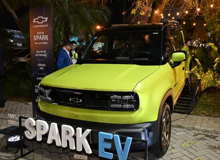 Coche Chevrolet Spark EV de color verde brillante con dos personas en traje y ambiente elegante con luces nocturnas.