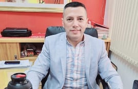 Hombre con cabello corto y blazer claro sonríe en oficina, junto a un cartel que indica su cargo como Director de Catastro.