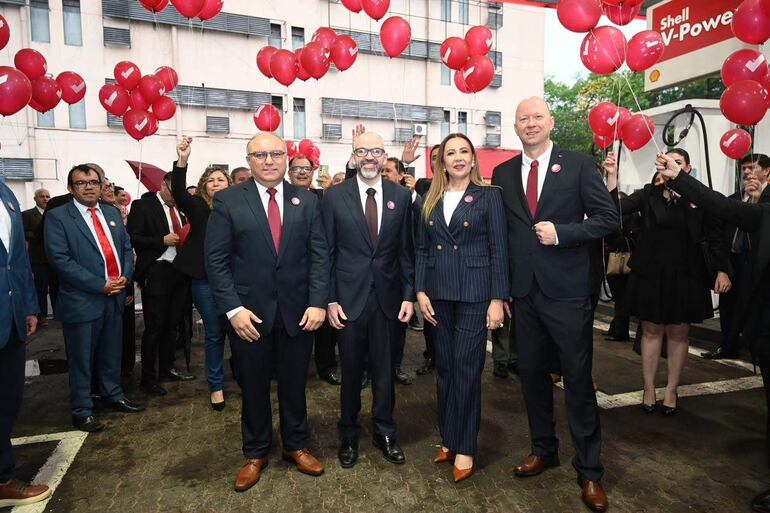 Enrique Javier Berni Brítez en traje oscuro y corbata roja, sonriente, junto a otros candidatos en un ambiente festivo con globos rojos.