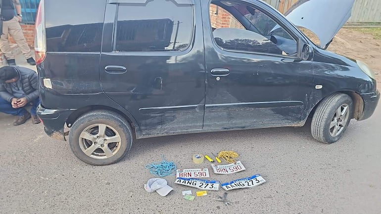 Hombre con abrigo oscuro sentado en el suelo, rodeado de objetos dispersos, mientras un policía lo observa de pie.