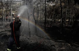 Un bombero rocía agua sobre un tronco de árbol quemado durante un incendio forestal en el pie norte de la montaña Hymettus en Atenas, Grecia. (Ilustrativa).