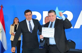 Alcides Riveros sonríe levantando un puño, mientras un hombre serio le entrega un documento en un evento del PLRA.