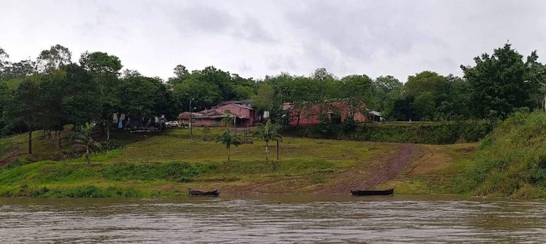 Costa verde junto al río Paraná rodeada de vegetación y casas rosadas, con embarcaciones en la orilla, sin personas presentes.