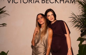 Nadia Ferreira con vestido plateado y cabello suelto, junto a Victoria Beckham, embarazada y con vestido púrpura, sonríen ante un fondo decorado.