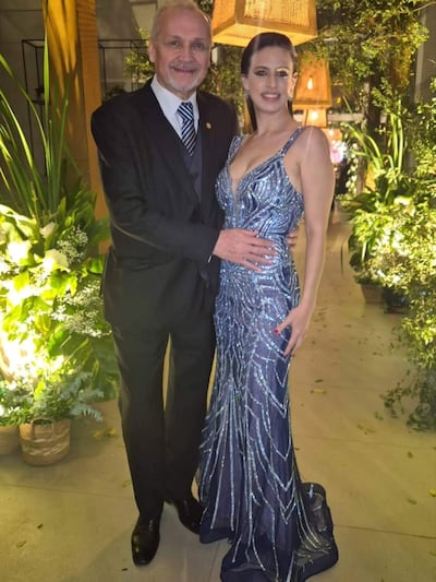 Mario Ferreiro con traje de gala, abrazando a una mujer en un vestido azul brillante entre plantas y luces tenues.