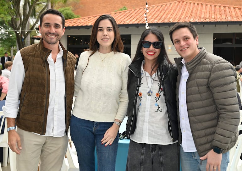 Cuatro personas sonrientes en un patio; hombres con atuendos informales y mujeres en prendas coloridas y elegantes.