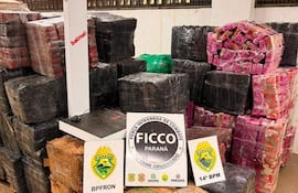 Paquetes envueltos en plástico negro y de colores, con letreros de la Policía Militar en un ambiente cerrado.