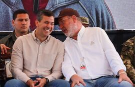 El presidente Santiago Peña (izq) sonriente conversa con el director de Itaipú, Justo Zacarías.