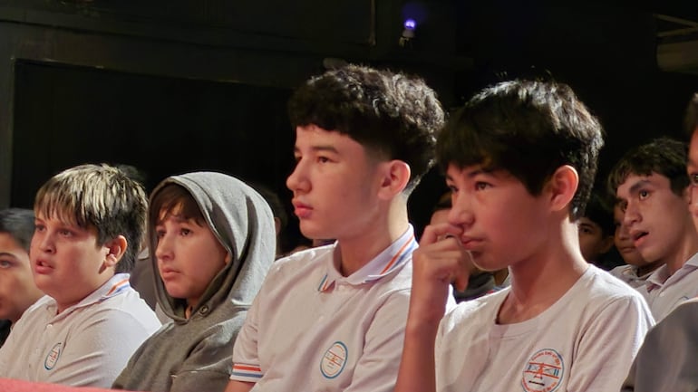Grupo de adolescentes en el auditorio Paraná, atentos y concentrados, visten camisetas blancas con un logo circular.