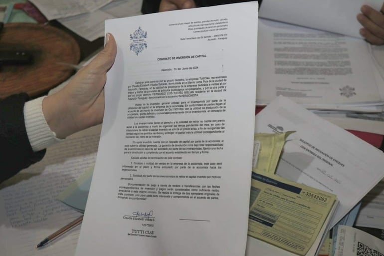 Documento de inversión firmado por Claudia Elizabeth Vitalba Salcedo, sostenido por una mano en un entorno desordenado.