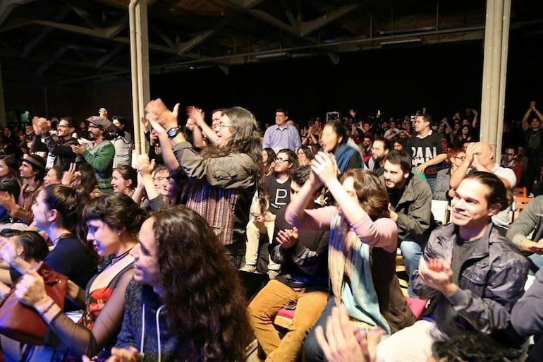 Grupo de personas aplaudiendo en un ambiente oscuro, mostrando alegría y concentración durante el homenaje a Hermeto Pascoal.