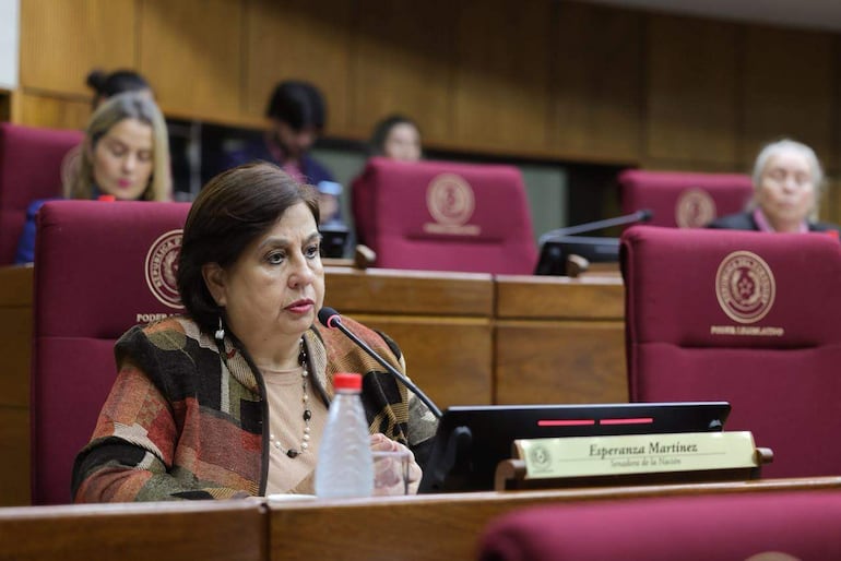 Esperanza Martínez, vestida con atuendo colorido, habla al micrófono en un ambiente formal, rodeada de colegas atentos.