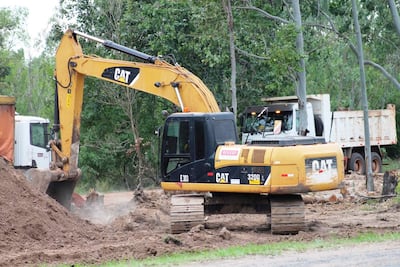 Excavadora amarilla CAT E303 en operación, con camión blanco cerca, en área de construcción rural rodeada de árboles.
