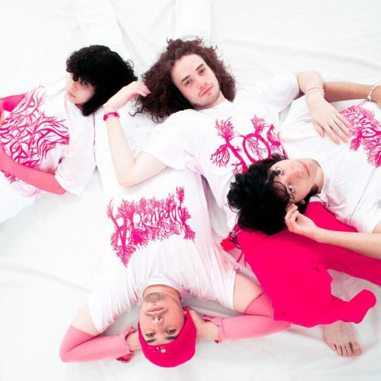 Cuatro personas recostadas sobre fondo blanco, luciendo camisetas blancas con detalles rosas, en una atmósfera artística y relajada.