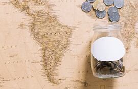 Imagen de un mapamundi, con un frasco de monedas abierto y moneas esparcidas sobre la parte del mapa que muestra Europa.
