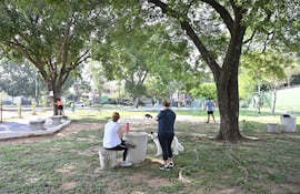 Niña en camiseta rosa escala un árbol; mujeres en camisetas blanca y azul comparten un espacio cercano, en un parque iluminado.