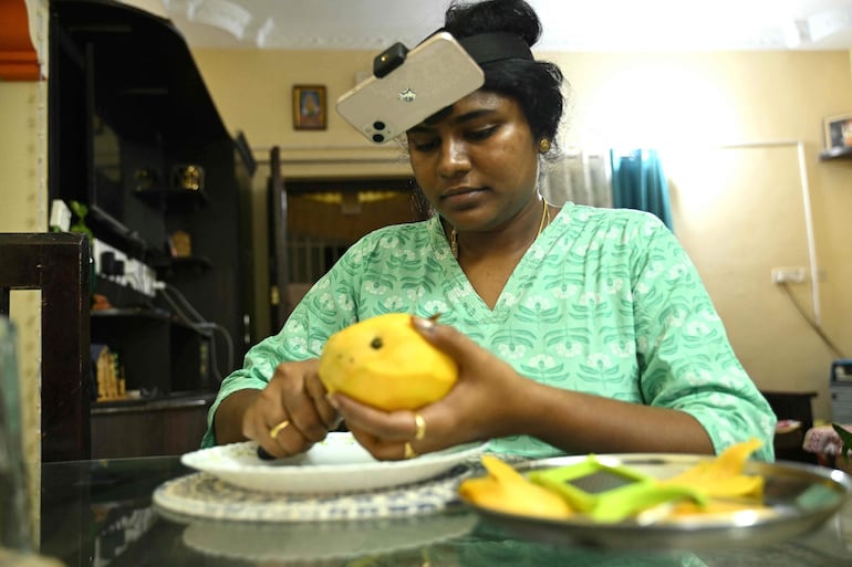 Esta fotografía, tomada el 15 de mayo de 2026, muestra a la ama de casa india Nagireddy Sriramyachandra usando un teléfono inteligente sujeto a la cabeza mientras registra sus acciones mediante captura de movimiento al cortar mangos en su casa de Chennai.