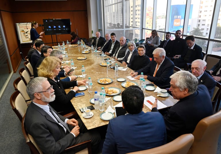 Linda Taiyen, Esteban Morábito y otros consules en una mesa rectangular, algunos escriben, otros escuchan atentamente, ambiente formal.