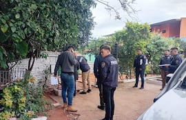 Grupo de hombres con chaquetas oscuras, uno habla por teléfono mientras otros revisan documentos en escenario urbano.