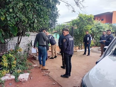 Grupo de hombres con chaquetas oscuras, uno habla por teléfono mientras otros revisan documentos en escenario urbano.