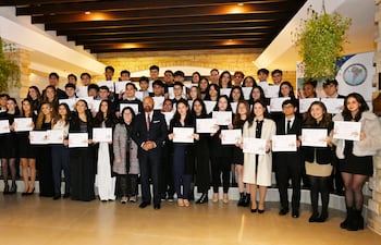 Grupo de graduados en vestimenta formal, sosteniendo diplomas, en un ambiente elegante con iluminación suave y decoración moderna.