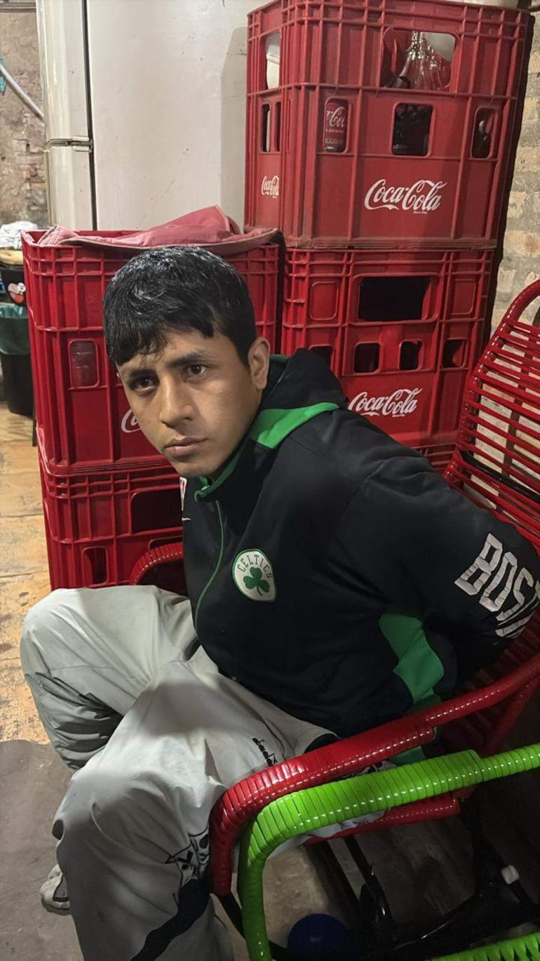 Persona sentada en silla verde con chaqueta negra y detalles verdes, mirando a la cámara en un ambiente sencillo.