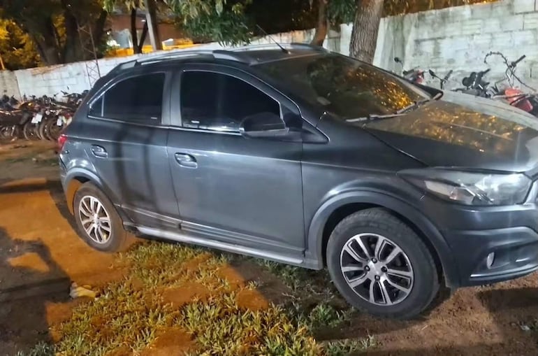Automóvil gris oscuro con ventanas tintadas, estacionado entre bicicletas, en un entorno de césped y tierra.