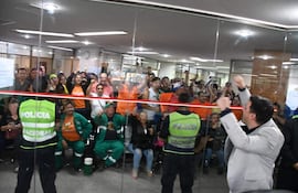 Cinco policías en chalecos verdes controlan el acceso, mientras una multitud expresa emociones diversas en un ambiente tenso.