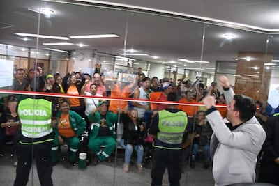 Cinco policías en chalecos verdes controlan el acceso, mientras una multitud expresa emociones diversas en un ambiente tenso.