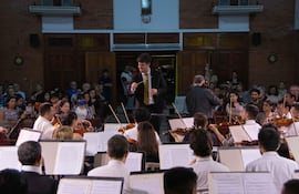 Director José Miguel Echeverría con batuta al frente de la orquesta, mientras el público observa atentamente en un ambiente acogedor.