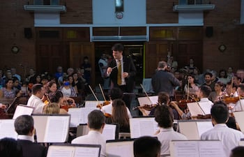 Director José Miguel Echeverría con batuta al frente de la orquesta, mientras el público observa atentamente en un ambiente acogedor.