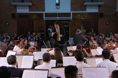 Director José Miguel Echeverría con batuta al frente de la orquesta, mientras el público observa atentamente en un ambiente acogedor.