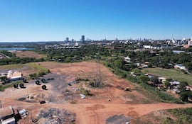 Paisaje urbano con terreno despejado, maquinaria y estructuras metálicas bajo un cielo azul en costanera de Asunción.